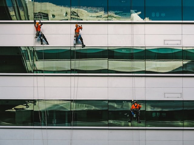 Two climbers cleaning the side of a building discussing pay per lead commercial cleaning